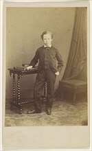 little boy in suit standing at a table with books on top; Joseph Brown, British, active 1860s, about 1869; Albumen silver print