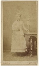 small woman standing, holding a vase on a table; C. Rummel, German, active Landau, Germany 1870s, 1870 - 1875; Albumen silver