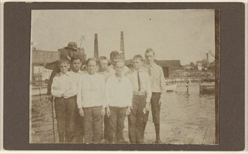 Eight young men standing on a dock near a river, with a man wearing a hat; 1875 - 1885; Albumen silver print