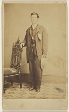 man standing holding his hat in one hand and holding a chair back with the other; Lew Horning, American, active Philadelphia