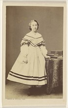 woman standing near a table with books on top; Bayard & Bertall; 1865 - 1875; Albumen silver print