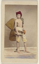 boy wearing native costume with baskets on back and carrying a water jug and small basket, standing; Giorgio Conrad, Italian