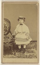 little girl wearing a pill-box hat, standing, holding the arm of a chair; Churchill & Denison; 1865 - 1875; Albumen silver print
