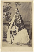 woman wearing a long dress with a dark shawl, standing, holding a bonnet; W. Hilliger, German, active Bad Homburg, Germany 1860s