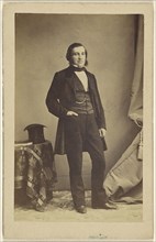 man standing with his hand in his pocket, a top hat on a table nearby; French; 1862; Albumen silver print