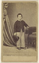 little boy standing, holding his cap, with hand on chair back with tassels; H. Jaeger & Company; 1865 - 1875; Albumen silver