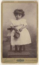 little girl standing in a chair, holding a pail with a ship on it; Armand; 1880 - 1890; Gelatin silver print