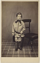 lttile boy standing near a chair, holding his cap; 1865-1875; Albumen silver print