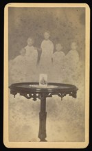 Five  spirits  in background with a photograph at center of table with a doily; William H. Mumler, American, 1832 - 1884