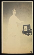 Female  spirit  with a carte-de-visite on a table propped against an album; Attributed to William H. Mumler, American, 1832