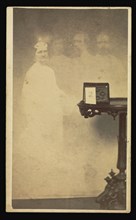 Female  spirit  with three male  spirits  next to table with a cabinet card propped against an album; Attributed to William H