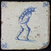 Occupation tile, blue with an image of man with large package on his back, corner motif of ox's head, wall tile tile sculpture