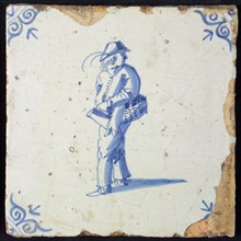 Occupation tile, blue with man carrying basket on the arm, looking back, corner motif of ox's head, wall tile tile sculpture