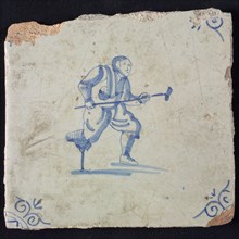 Figure tile, blue with man with wooden leg and crutch, in attacking position, corner motif oxen head, wall tile tile sculpture