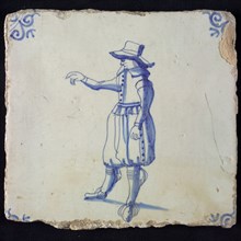 Figure tile, blue with standing man pointing with right hand, breeches and big hat, corner pattern ox head, wall tile