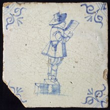 Figure tile, blue with man with big hat standing on an elevation, reads from sheet of paper, corner motif oxen head, wall tile