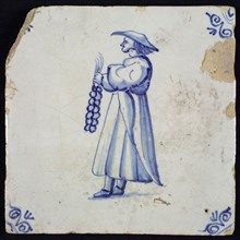 Figure tile, blue with standing figure with long cloak or dress and string of garlic in the hand, corner pattern ox head, wall