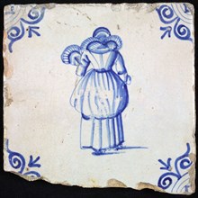 Figure tile, blue with lady with lace collar, fan and included overcoat, seen on the back, corner pattern ox head, wall tile