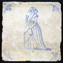 Figure tile, blue with lady with fan, lifts her skirt with hand, corner motif of ox's head, wall tile tile sculpture ceramic