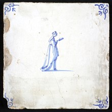 Figure tile, blue with lady with long dress with drag with mirror or fan in hand, corner pattern ox head, wall tile