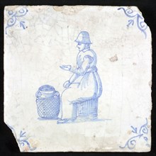 Figure tile, blue with woman sitting on chest with milk jug for her on the ground, corner motif oxen head, wall tile
