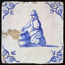 Figure tile, blue with sitting woman with barrel in front of her and bag next to her, corner motif ox's head, wall tile