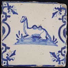 Animal tile, lying camel to the left on plot between balusters, in blue on white, corner pattern French lily, wall tile