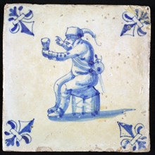 Figure tile, blue with man sitting on stool with cup in hand, corner pattern lily, wall tile tile sculpture ceramic earthenware