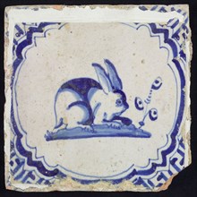 Animal tile, hare to the right on ground within scalloped frame with braces, in blue on white, corner motif meanders, wall tile