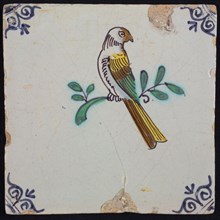Animal tile, bird on branch to the left in yellow, purple, brown, green and blue on white, corner pattern ossenkop, wall tile