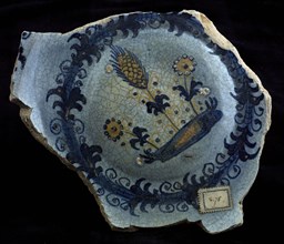 Fragment majolica dish, yellow and blue on white, flowers and ear of corn on piece of land, plate crockery holder soil find