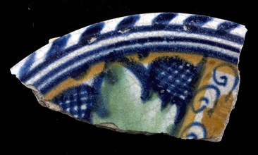 Fragment of majolica dish, orange and green and blue on white, cross shape and in between leaves, in the middle circles, cable