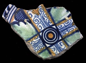 Fragment of majolica dish, orange and green and blue on white, cross shape and in between leaves, in the middle circles, cable