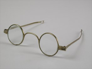 Glasses with round lenses on strength, frame of brass with wide bridge and hinged springs that end in loop shape, spectacle eye