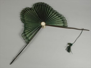 Parasol fan, two thin dark brown wooden legs, leaf shaped fan leaf of green silk with green edge around it, legs knots, cord and