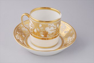 White cup and saucer with gold colored band with acorn and leaf decoration, cup and saucer drinking utensils tableware holder