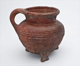 Pottery cooking jug on three claw feet, rotations on shoulder and one ear, sparingly glazed, grape cooking pot crockery holder