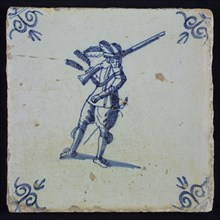 White tile with blue warrior with plume hat and gun, looks surprised; corner pattern ox head, wall tile tile sculpture ceramics