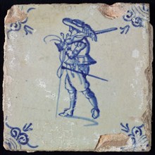 White tile with blue warrior with hat, rifle and stand; corner pattern ox head, wall tile tile sculpture ceramic earthenware