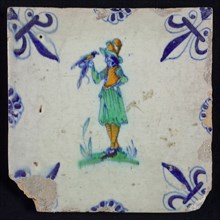 White tile with standing man with bird in yellow, green and blue, corner pattern french lily in blue and border decoration