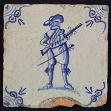 White tile with blue warrior with rifle and hat, seen from behind; corner pattern ox head, wall tile tile sculpture ceramic