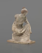 Terracotta figurine of a girl throwing dice. Female figurine of a crouching girl throwing dice;