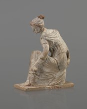 Terracotta figurine of a girl throwing dice. Female figurine in a long, finely pleated sleeveless