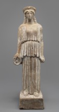 Female terracotta figurine of a standing woman positioned frontally on a quadrangular base. The