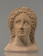 Votive female head, female head wearing a wreath, from under which lush locks of hair curl down the