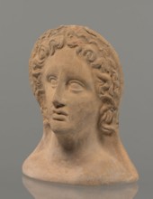 Votive female head, female head wearing a wreath, from under which lush locks of hair curl down the