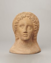Votive female head. Female head wearing a wreath, from under which lush locks of hair curl down the