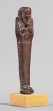 Ushabti, A shabti figurine dressed in a shroud stands on a base. On the head is a smooth wig