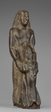 Figurine of a priest holding a statuette of the god Osiris. The priest stands, holding the