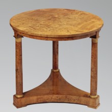 Round table on three legs in the form of slender columns with smooth shafts, mounted on a
